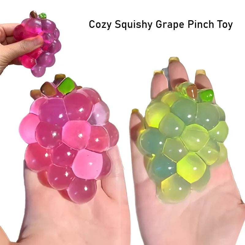 A hand is holding a colorful squishy grape pinch toy with translucent pink and green fruit shapes.