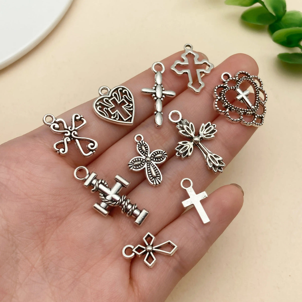 A hand holds various vintage silver cross charms and heart pendants for jewelry making