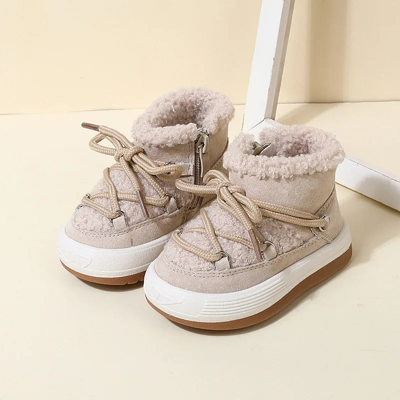 A pair of beige baby winter snow boots with plush lining and rubber soles resting on a light surface.