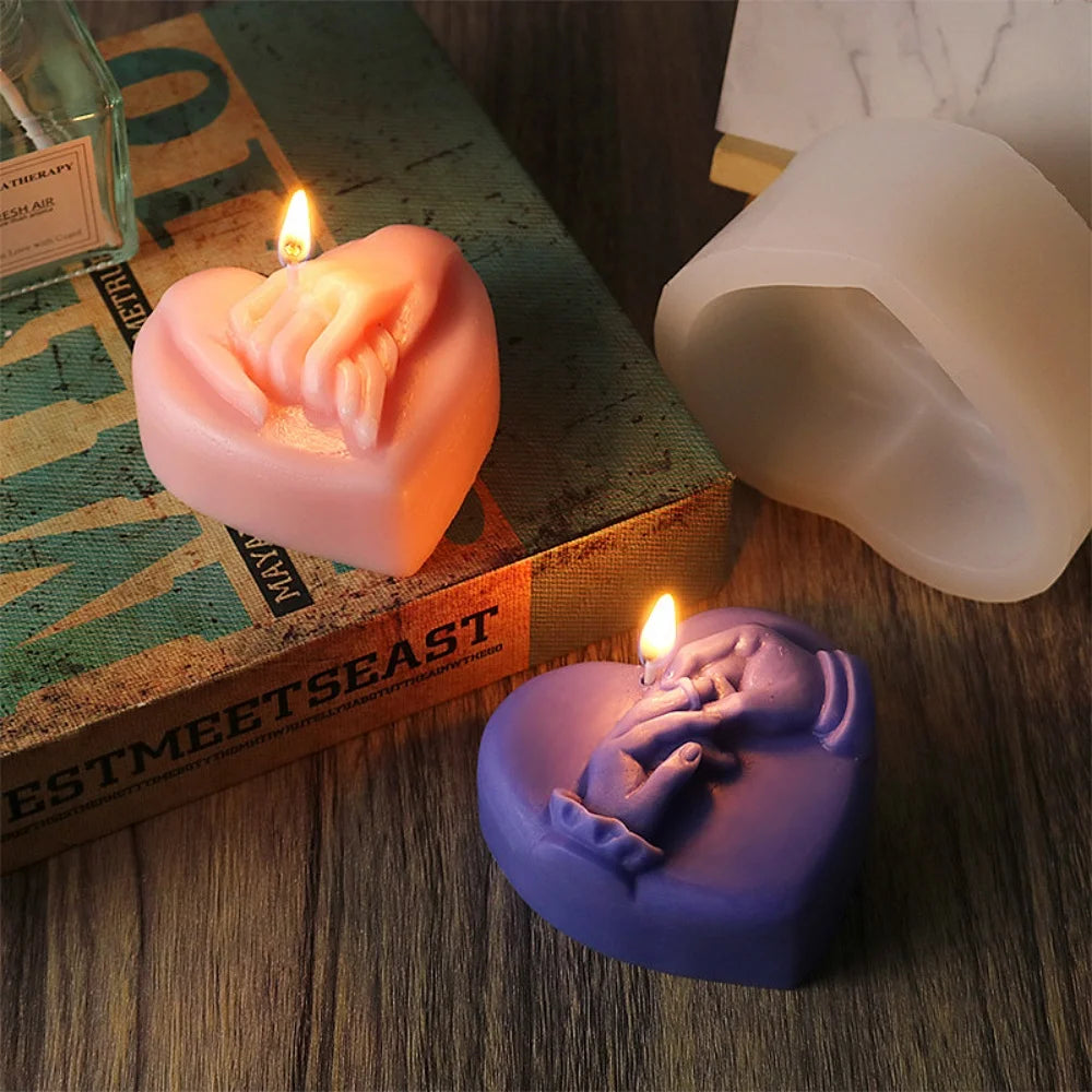 A pink heart-shaped silicone mold for candles resting on a green book with a lit candle.