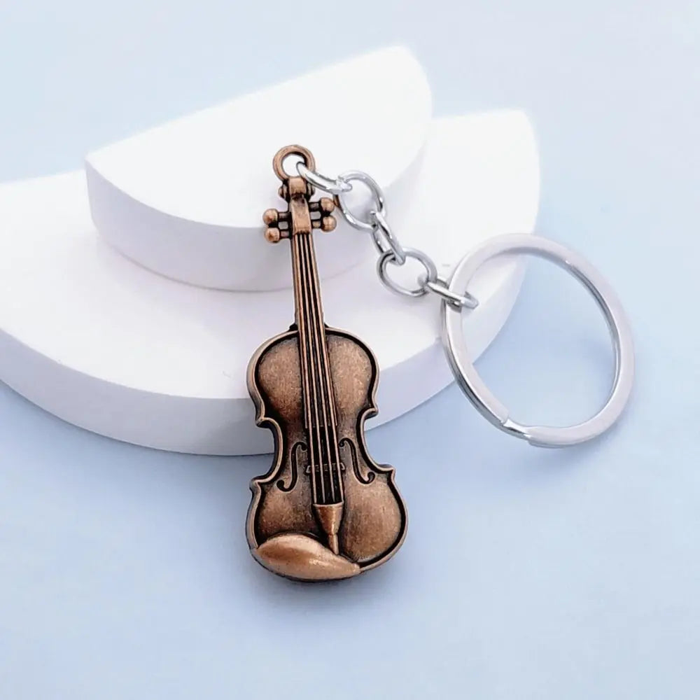 A vintage brown violin charm attached to a silver chain and keyring, resting on a white surface.