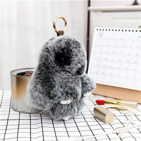 A fluffy gray plush bunny keychain resting on a black and white grid surface.
