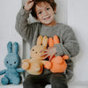 A smiling young boy holding several Miffy plush toys in various orange and yellow colors.