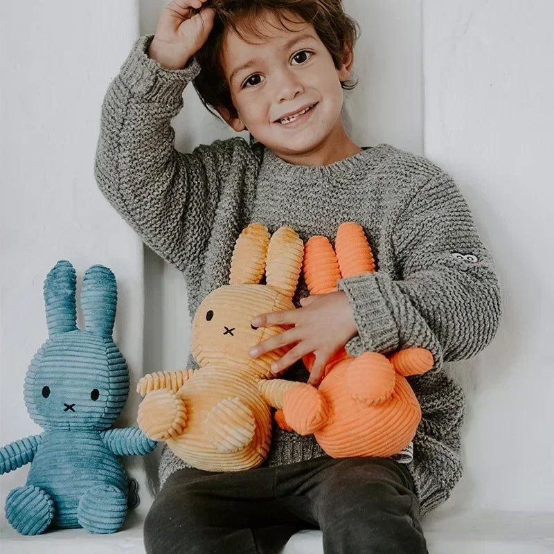 A smiling young boy holding several Miffy plush toys in various orange and yellow colors.