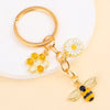 Gold enamel flower keychain featuring a bee and a daisy on a white background.