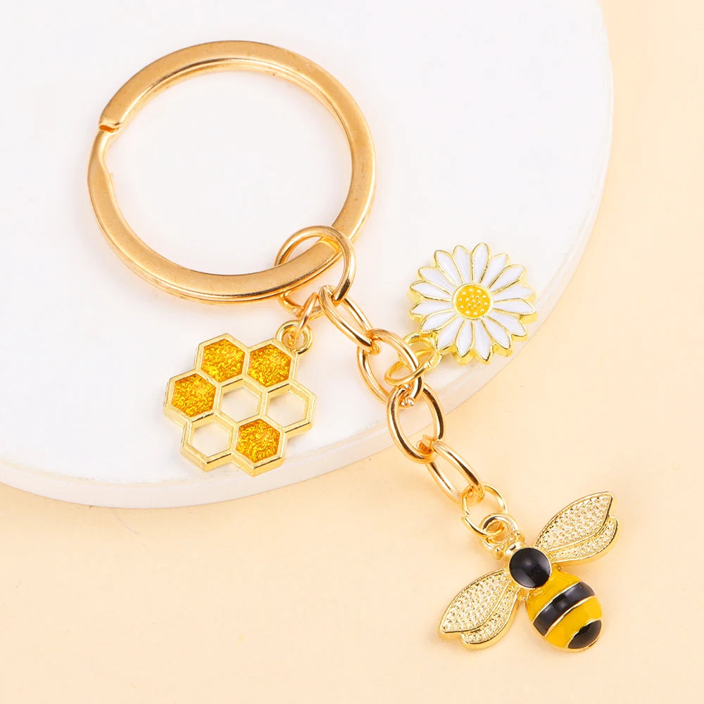 Gold enamel flower keychain featuring a bee and a daisy on a white background.