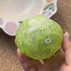 A hand holds a translucent lime green stress ball with small glittery stars and an apple design against a blurred background.
