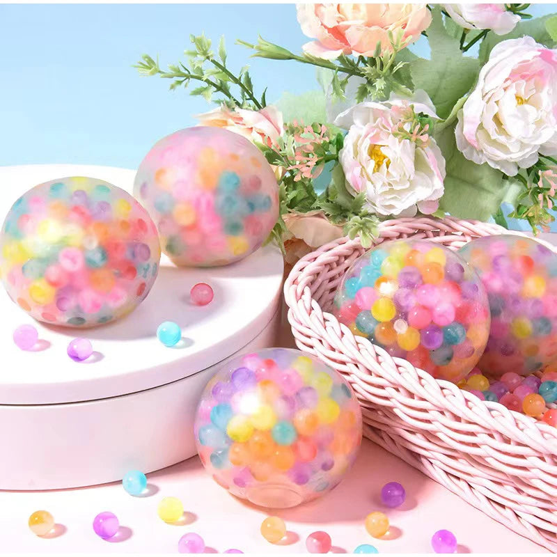 A collection of colorful squeeze stress relief balls with mesh netting arranged on a pink surface.