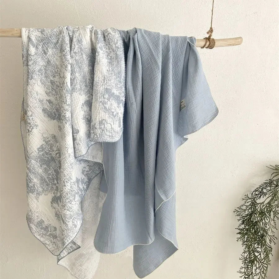 A light blue muslin swaddle blanket with a floral print hanging on a wooden rack.