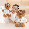 A young woman is holding a fluffy brown bear plush toy dressed in a white outfit and an eye mask.