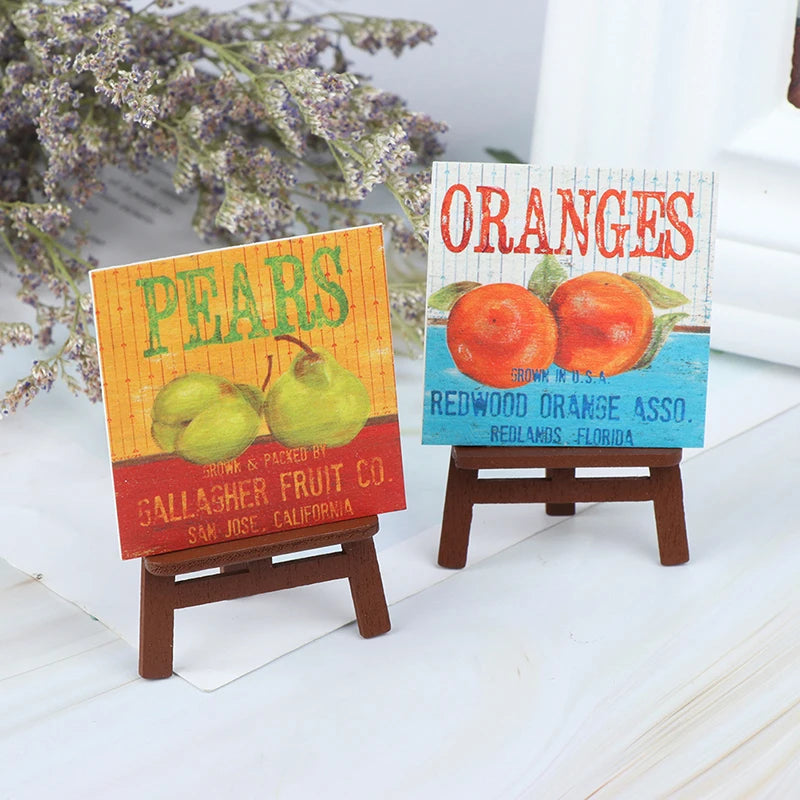 Two wooden signs featuring pears and oranges displayed on miniature artist easels.