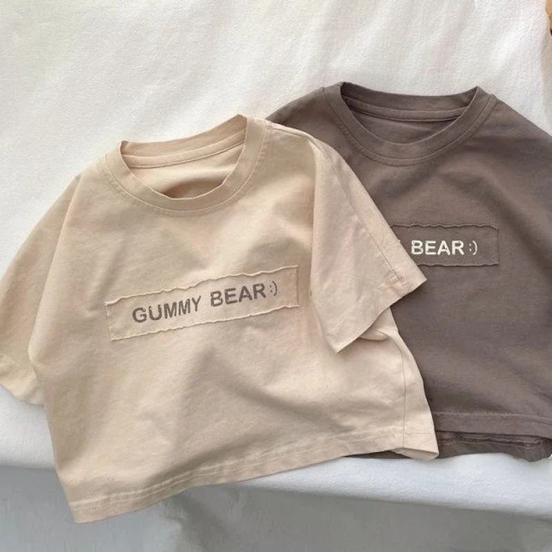 A light beige short-sleeve t-shirt with the text GUMMY BEAR printed on the chest, shown flat lay.