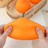 A hand is squeezing an orange fruit squishy stress relief fidget toy against a light background.