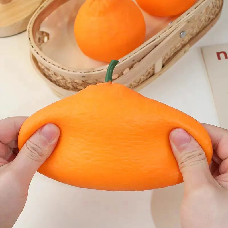 A hand is squeezing an orange fruit squishy stress relief fidget toy against a light background.