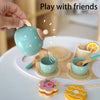A hand is pouring liquid from a wooden pretend coffee maker into small cups and accessories on a white plate.