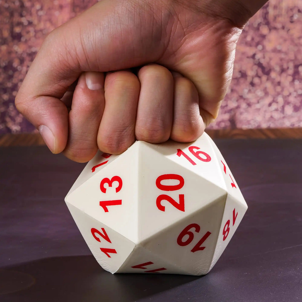 A hand holds a white D20 polyhedral dice on a dark surface.