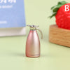 A small, rose gold miniature alloy kettle is shown on a light green surface next to a wooden block and a strawberry.