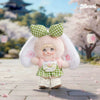 A fluffy pink plush keychain with green checkered ears and a white dress, standing on a paved surface.