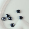A collection of ten glossy black heart-shaped ceramic beads arranged on a white surface.