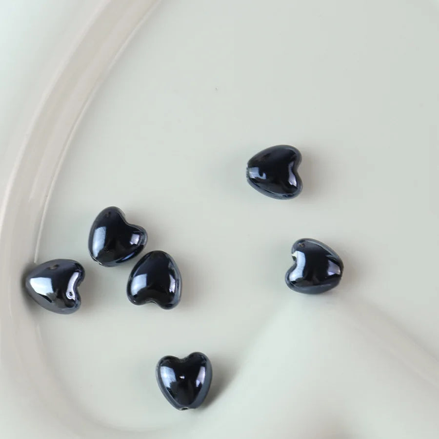 A collection of ten glossy black heart-shaped ceramic beads arranged on a white surface.