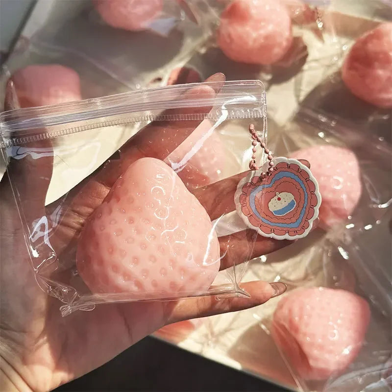 A hand holds a clear plastic bag containing a pink strawberry squishy toy.
