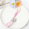A soft pink bunny plush keychain with a yellow bow charm resting on a white plate next to a light blue flower.