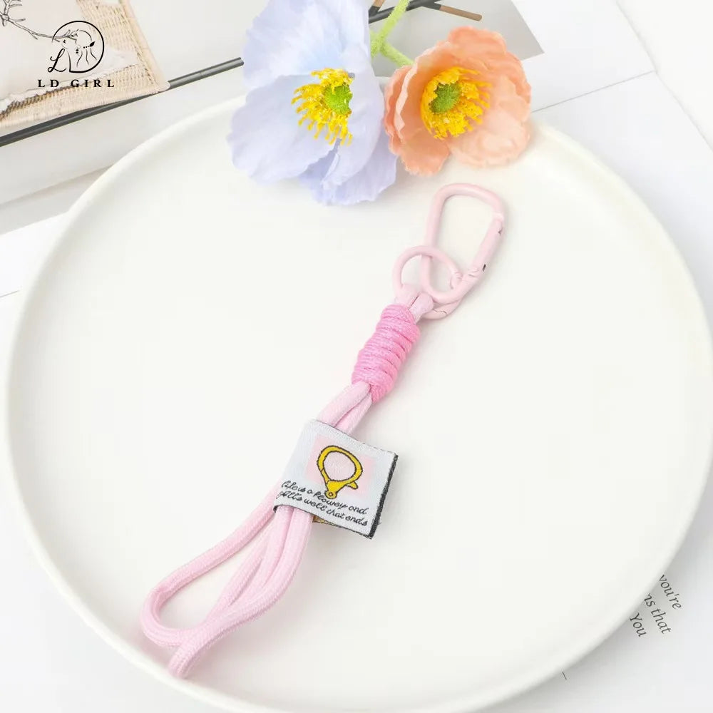 A soft pink bunny plush keychain with a yellow bow charm resting on a white plate next to a light blue flower.