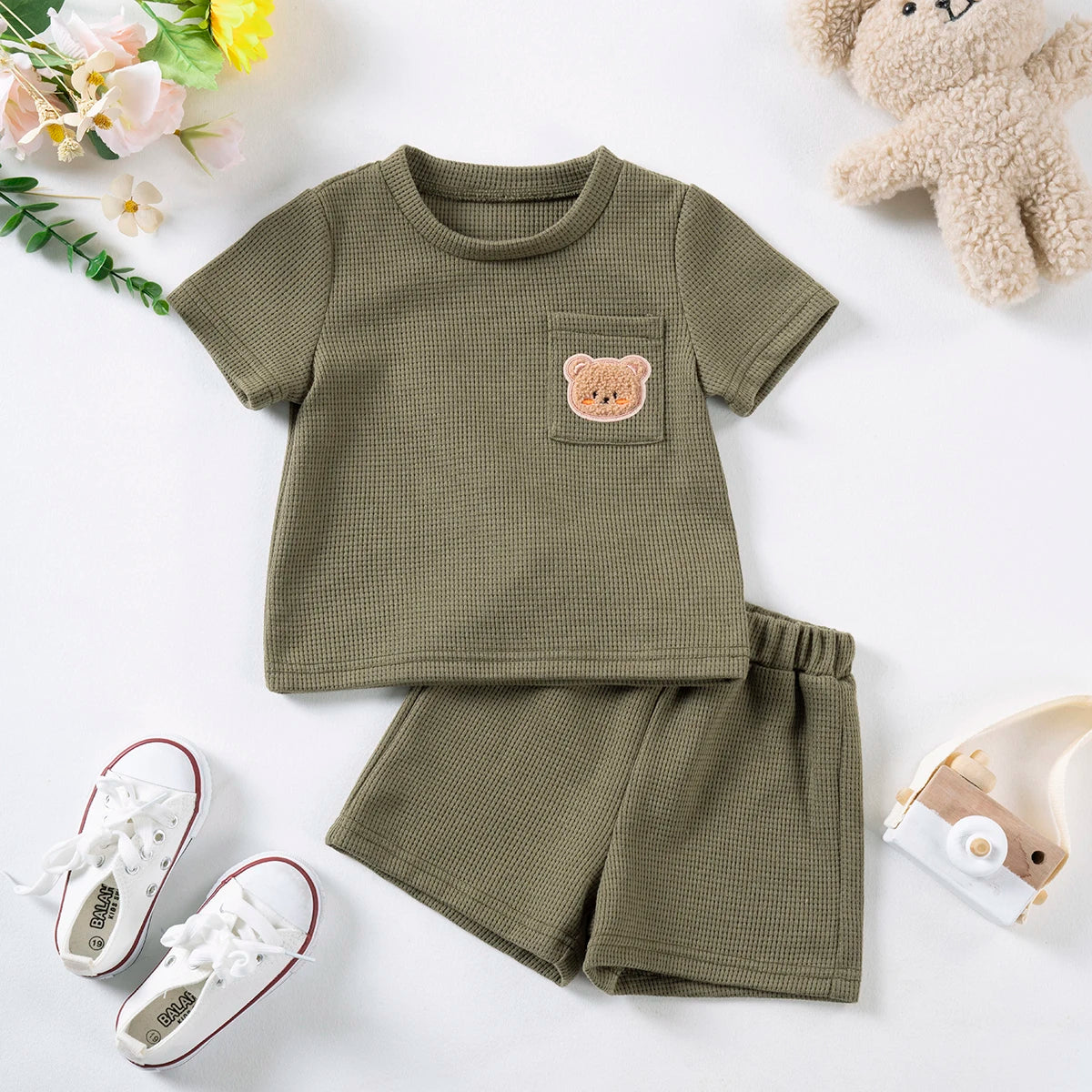 A set of olive green baby clothing featuring a short-sleeved t-shirt with a bear print and matching shorts.