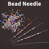 A collection of ultra-fine metal bead needles with colorful beads scattered and laid out on a dark surface.