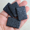 A hand holds a set of miniature black textured toy food items, including beef steak and pasta, for a dollhouse.