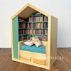 A wooden miniature bookshelf decor set with green shelving filled with colorful books and a blue mat inside.