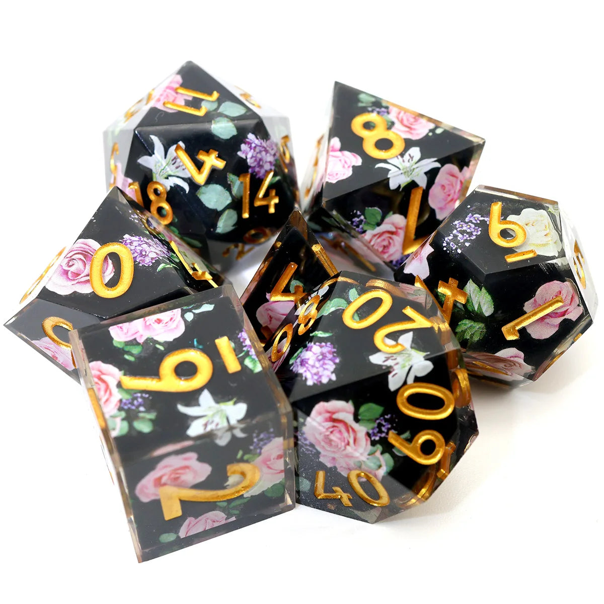 A set of seven black resin polyhedral dice with gold numbers and floral designs displayed on a white background.