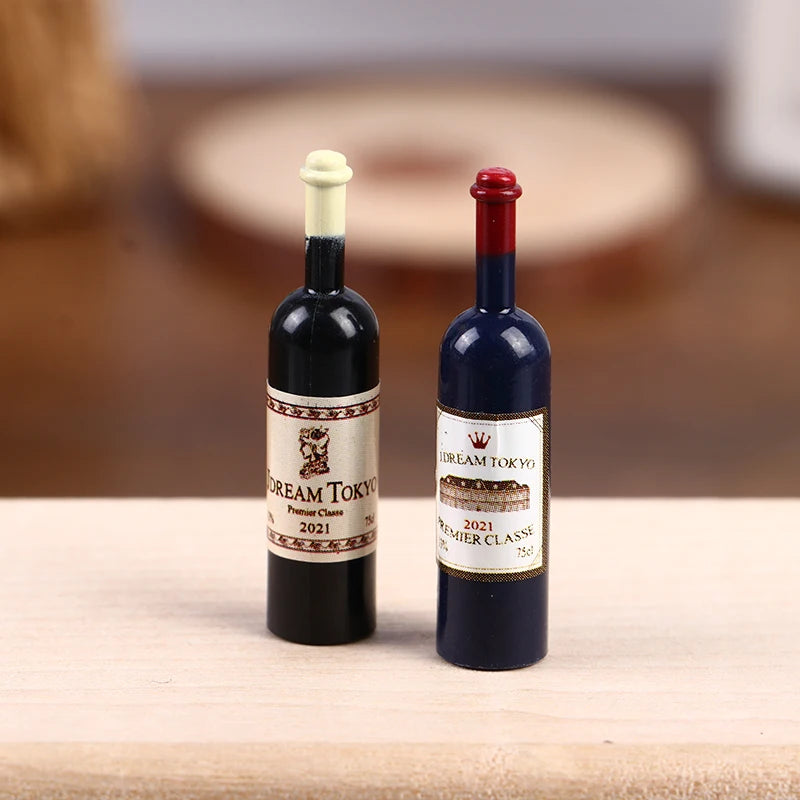 Two miniature resin wine bottles with gold closures and labels on a wooden surface.