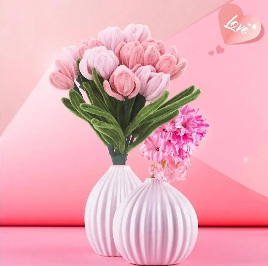 A bouquet of pink and light purple chenille craft flowers displayed in white ceramic vases against a pink background.