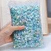 A hand holds a clear bag filled with multicolor aurora resin nail charms.