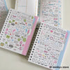 A collection of pink and white kawaii stickers in a spiral notebook for journaling and scrapbooking