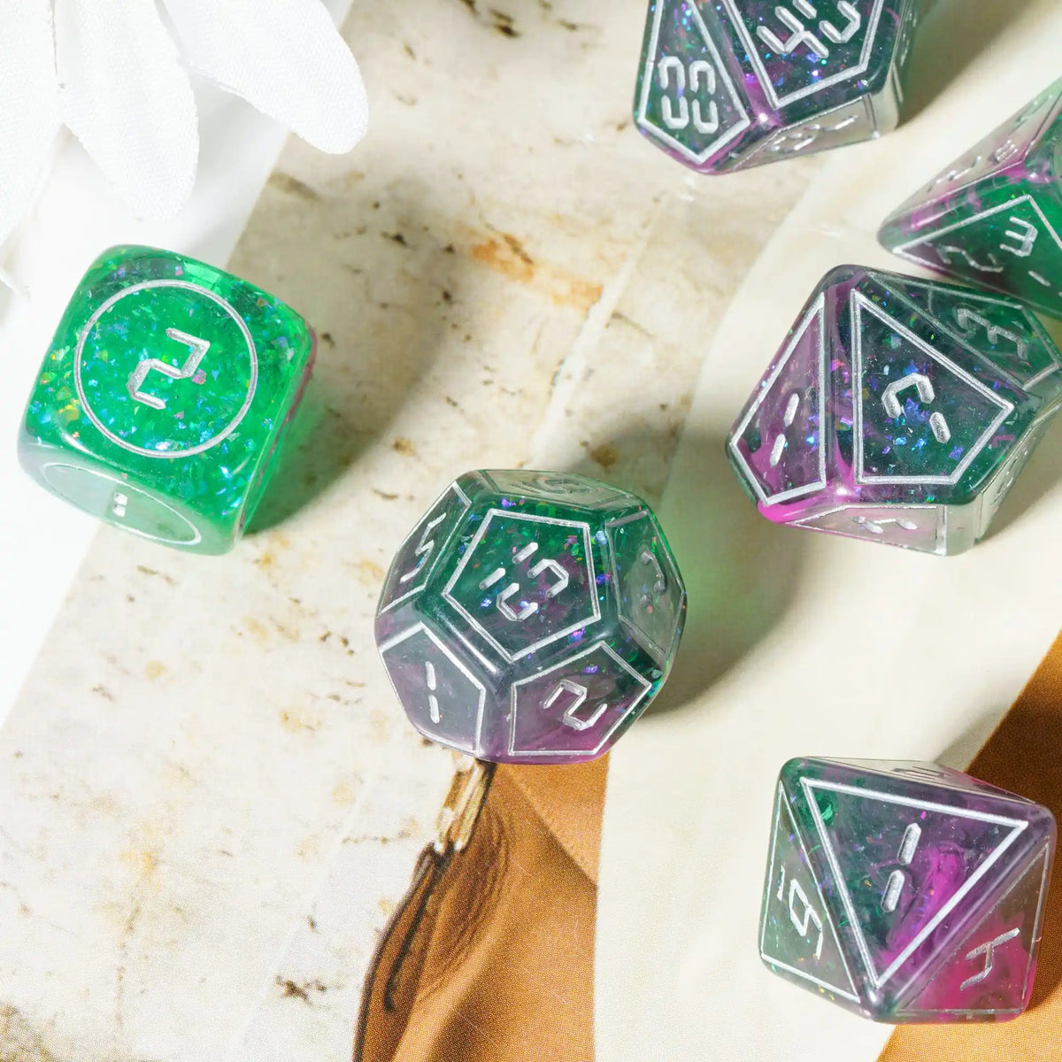 A collection of seven iridescent resin polyhedral dice set on a light marble surface.
