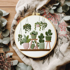 A DIY cross stitch starter kit featuring green potted plants embroidered on a circular wooden board.
