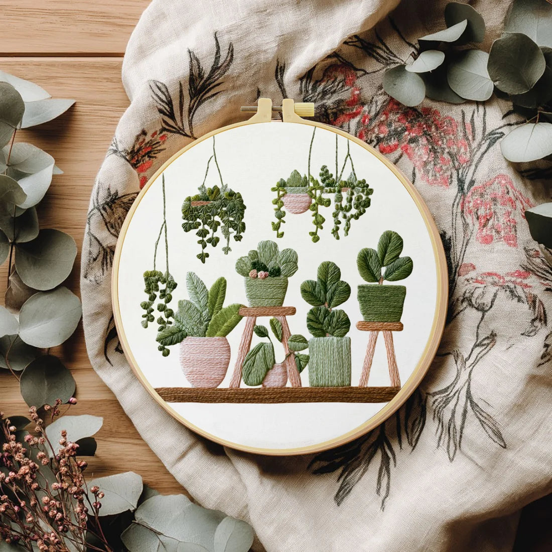 A DIY cross stitch starter kit featuring green potted plants embroidered on a circular wooden board.