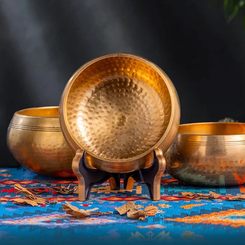 A handcrafted brass Tibetan singing bowl resting on a blue cloth with dried leaves.