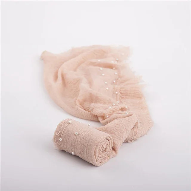 A soft, blush pink knit wrap for newborn photography featuring delicate pearl embellishments.