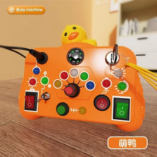 An orange Montessori busy board with various light switches and a yellow duck toy.