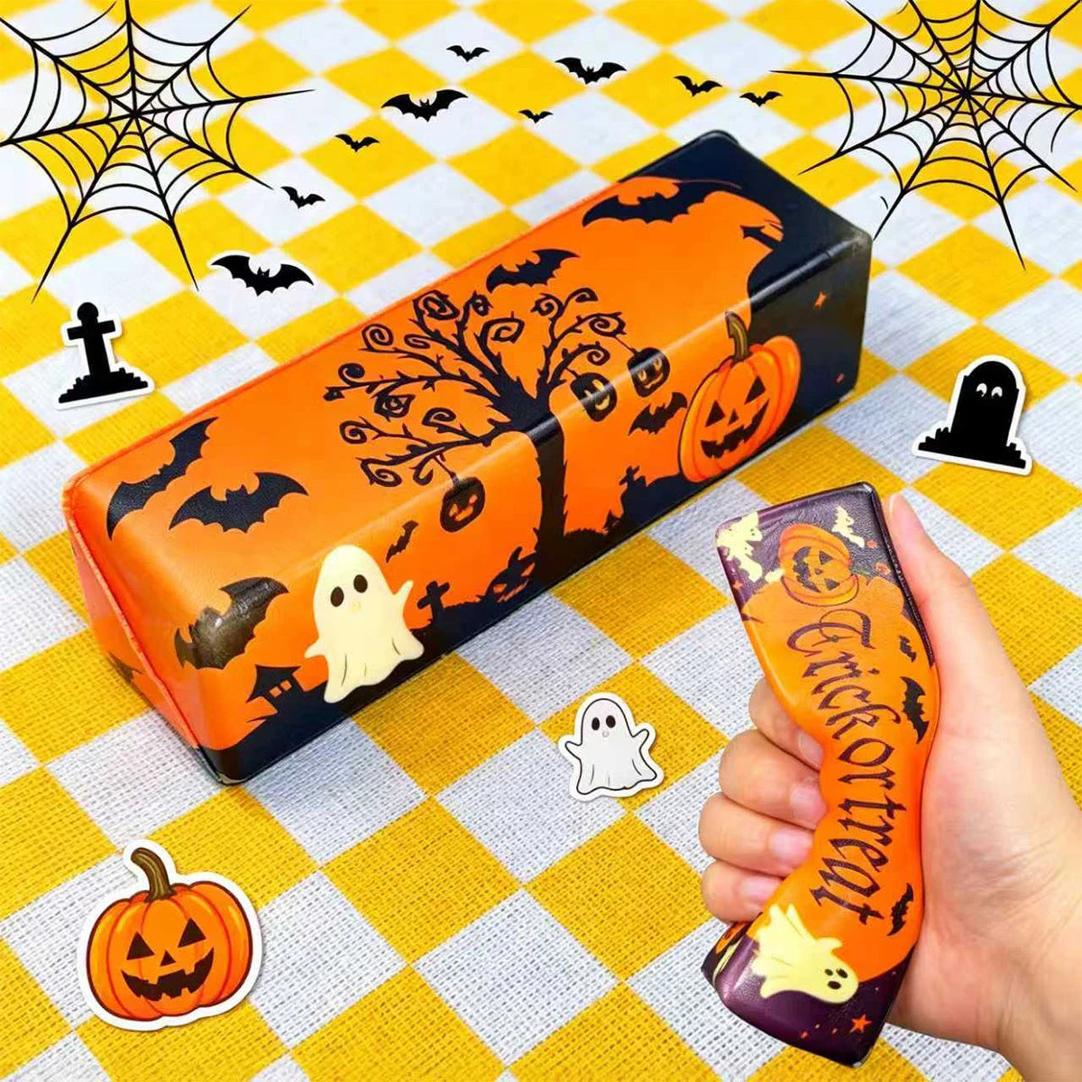 An orange Halloween butter squishy toy set featuring a pumpkin and ghost stress relief fidget on a yellow checkered surface.