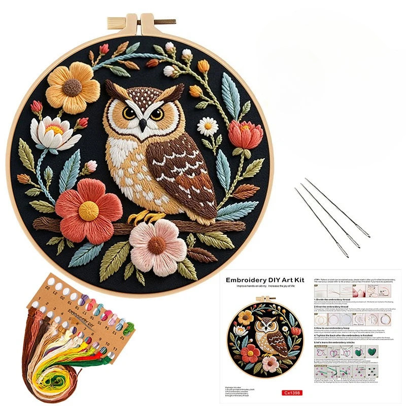 Embroidery kit featuring an owl and flower design on a wooden board with threads and tools.