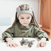 A young girl with braids is looking at a gray silicone toy airplane on a white table.