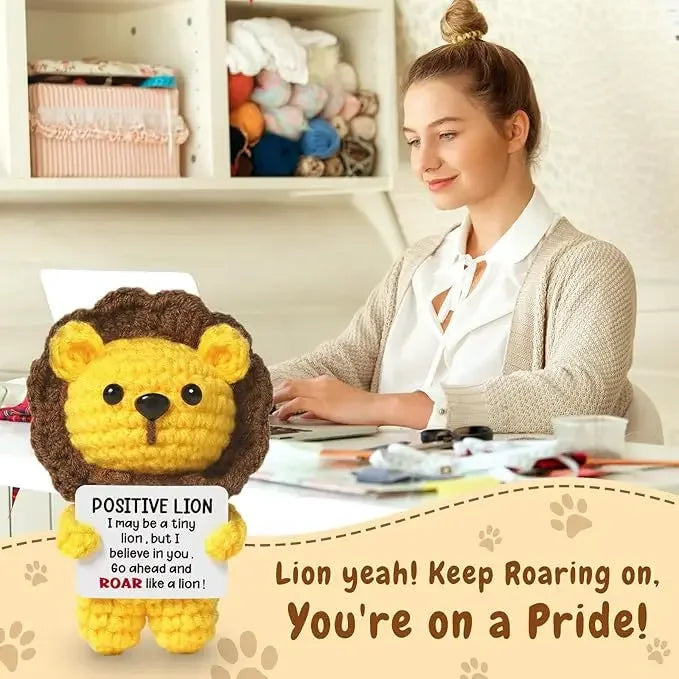 A yellow crochet lion doll with a positive message card is displayed on a white background.