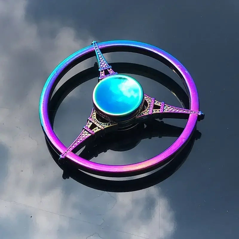 A colorful metal fidget spinner with a glowing blue center and purple accents, resting on a reflective surface.