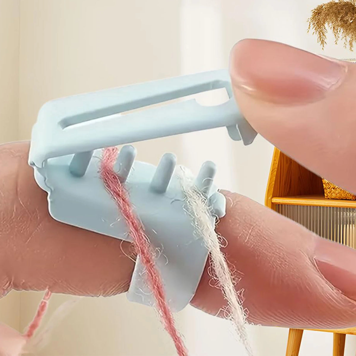 A hand holds a light blue ergonomic yarn guide ring, demonstrating its use for crochet and knitting.