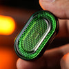 A hand holds a green metal mechanical fidget slider with a diamond pattern design.