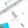 A white ballpoint pen with a silver beaded tip rests on a white surface next to a notebook.